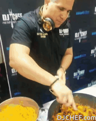 A Man Wearing Headphones Is Preparing Food In Front Of A Wall That Says Dj Chef GIF
