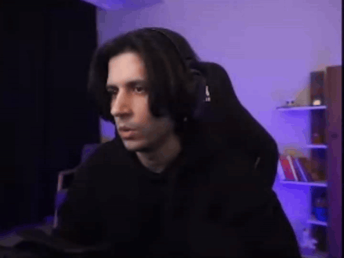 A Man Wearing Headphones Is Sitting In A Gaming Chair In Front Of A Computer . GIF