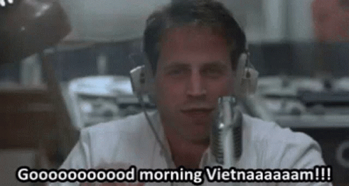 A Man Wearing Headphones Is Sitting In Front Of A Microphone And Saying Good Morning Vietnam . GIF
