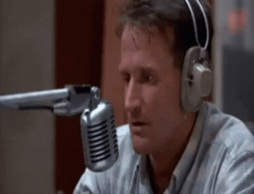A Man Wearing Headphones Is Sitting In Front Of A Microphone And Talking Into It . GIF