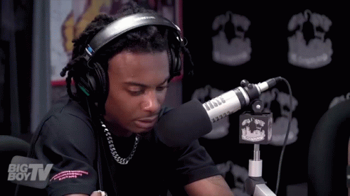 A Man Wearing Headphones Is Sitting In Front Of A Microphone That Says Big Tv On It GIF