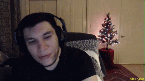 A Man Wearing Headphones Is Sitting In Front Of A Small Christmas Tree GIF