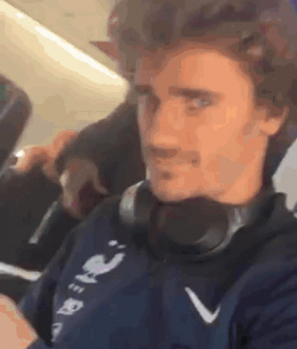 A Man Wearing Headphones Is Sitting On A Plane And Looking At His Phone . GIF
