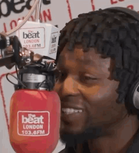 A Man Wearing Headphones Is Smiling In Front Of A Microphone In A Radio Station . GIF