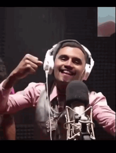 A Man Wearing Headphones Is Smiling In Front Of A Microphone . GIF