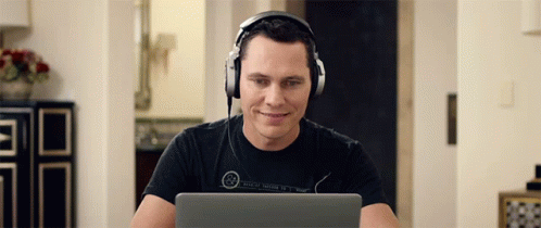 A Man Wearing Headphones Is Smiling While Looking At His Laptop GIF
