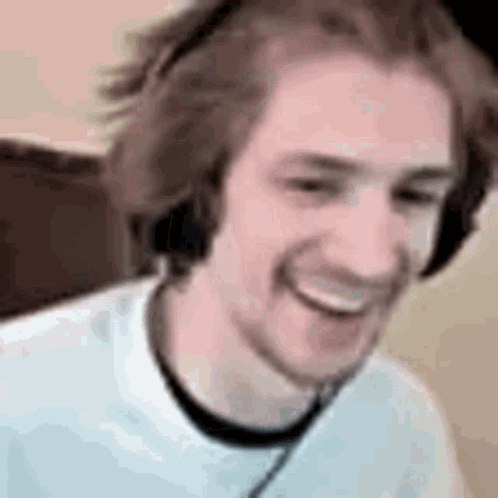 A Man Wearing Headphones Is Smiling While Sitting In Front Of A Computer . GIF