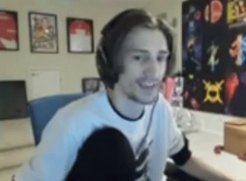 A Man Wearing Headphones Is Smiling While Sitting In Front Of A Computer In A Room . GIF