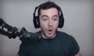 A Man Wearing Headphones Is Standing In Front Of A Microphone And Making A Funny Face . GIF