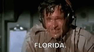 A Man Wearing Headphones Is Sweating While Sitting On A Plane And Saying `` Florida '' . GIF