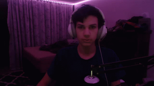 A Man Wearing Headphones Is Taking A Selfie In A Dark Room With Purple Lights Behind Him . GIF