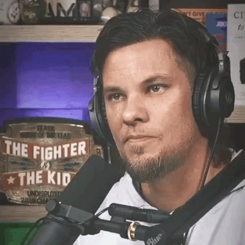 A Man Wearing Headphones Is Talking Into A Microphone With A Sign That Says The Fighter And The Kid GIF