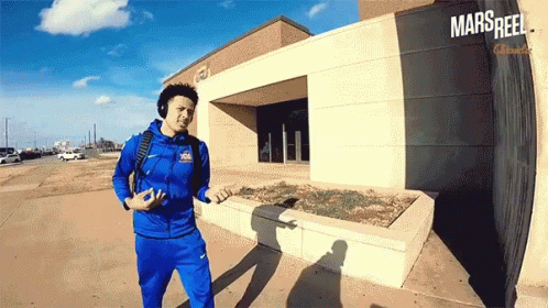 A Man Wearing Headphones Is Walking In Front Of A Building That Says Mars Reel On It GIF