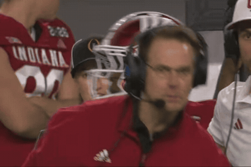 A Man Wearing Headphones Is Watching A Football Game With A Player Wearing A Jersey That Says Nebraska GIF
