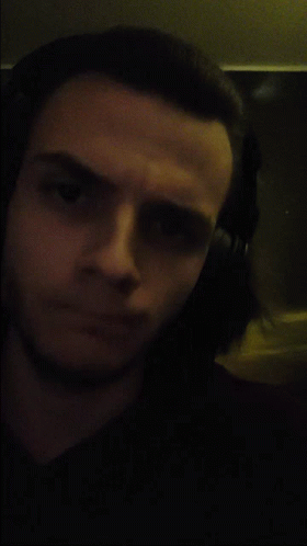 A Man Wearing Headphones Looks At The Camera In A Dark Room GIF