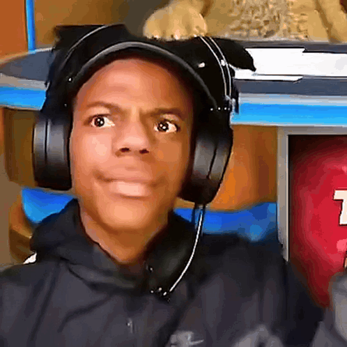 a man wearing headphones looks at the camera with a t on the wall behind him