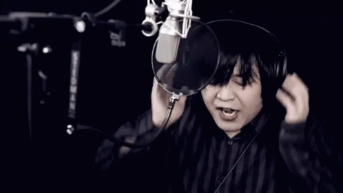 A Man Wearing Headphones Singing Into A Microphone With His Mouth Open GIF