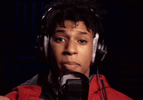 A Man Wearing Headphones Sings Into A Microphone In Front Of A Neon Open Sign GIF