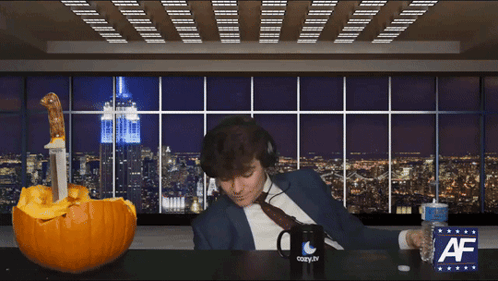 A Man Wearing Headphones Sits At A Table With A Cozy.tv Mug And A Pumpkin GIF
