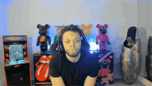 A Man Wearing Headphones Sits In Front Of A Pac Man Machine GIF