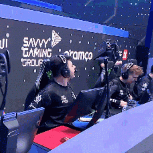 A Man Wearing Headphones Sits In Front Of A Savvy Gaming Group Sign GIF
