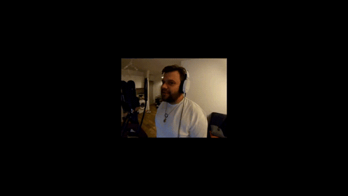 A Man Wearing Headphones Stands In Front Of A Black Screen GIF