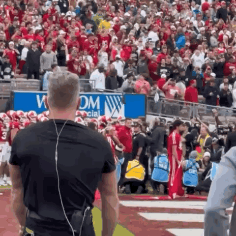 A Man Wearing Headphones Stands In Front Of A Crowd At A Football Game .. GIF