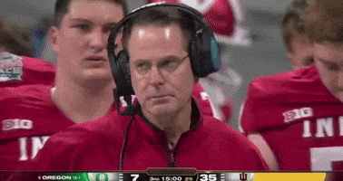 A Man Wearing Headphones Stands In Front Of A Group Of Football Players Wearing Red Jerseys That Say Big GIF
