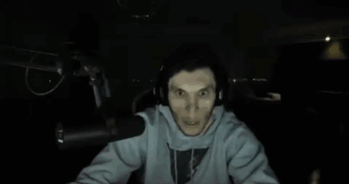 A Man Wearing Headphones Stands In Front Of A Microphone And Looks Surprised GIF
