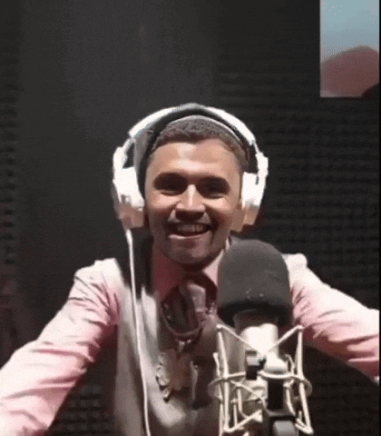 A Man Wearing Headphones Stands In Front Of A Microphone And Smiles GIF