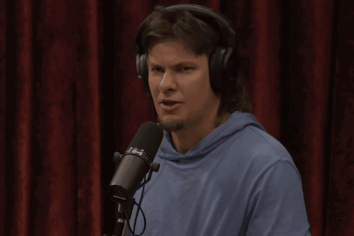 A Man Wearing Headphones Stands In Front Of A Microphone That Says ' Shure ' On It GIF