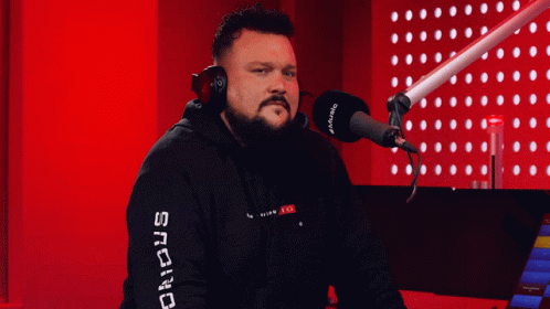 A Man Wearing Headphones Stands In Front Of A Microphone With The Word Snc On His Sleeve GIF