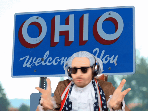 A Man Wearing Headphones Stands In Front Of A Sign That Says Ohio Welcome You GIF