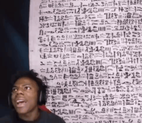 a man wearing headphones stands in front of a wall with ancient writing