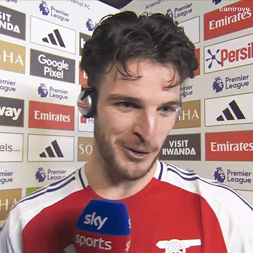 A Man Wearing Headphones Stands In Front Of A Wall With Emirates Logos On It GIF