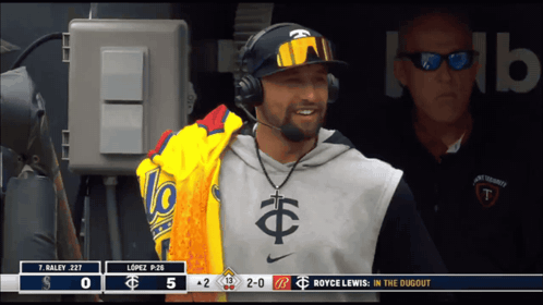 A Man Wearing Headphones Stands In The Dugout With A Scoreboard Behind Him That Says Royce Lewis In The Dugout GIF