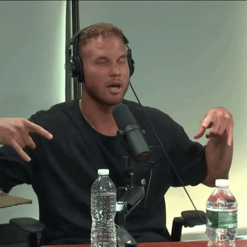 A Man Wearing Headphones Talking Into A Microphone With A Bottle Of Water In Front Of Him GIF