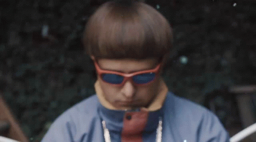 A Man Wearing Orange Sunglasses And A Blue Jacket Looks At The Camera GIF