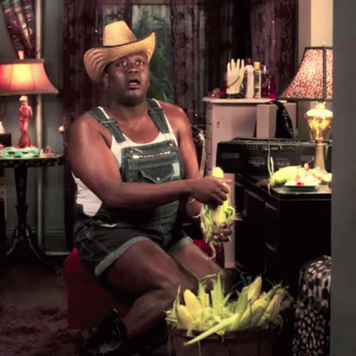A Man Wearing Overalls And A Cowboy Hat Holds Corn On The Cob In His Hands GIF