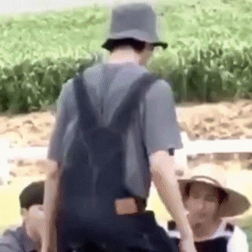 A Man Wearing Overalls And A Hat Is Standing In A Field With A Backpack . GIF