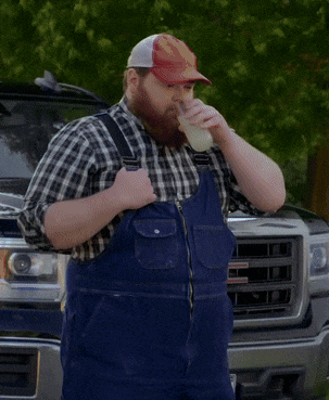A Man Wearing Overalls And A Hat That Says ' Gmc ' On It Drinks From A Cup GIF
