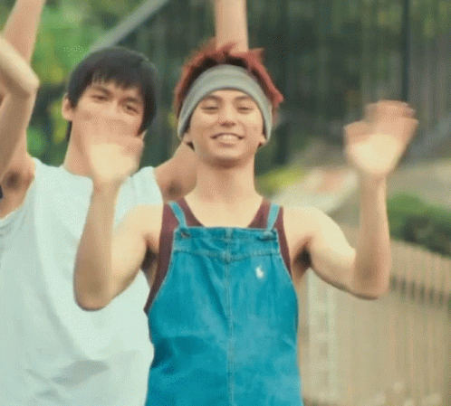 A Man Wearing Overalls And A Headband Is Waving At The Camera GIF