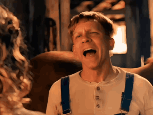 A Man Wearing Overalls And A White Shirt Is Making A Funny Face GIF
