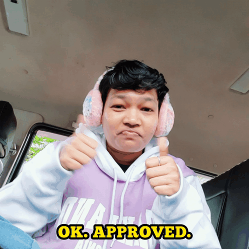 A Man Wearing Pink Ear Muffs And A Purple Hoodie Giving A Thumbs Up Sign GIF