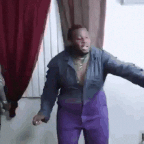 A Man Wearing Purple Pants And A Blue Jacket Is Dancing In A Room . GIF