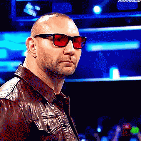 A Man Wearing Red Sunglasses And A Leather Jacket Is Standing In Front Of A Crowd . GIF