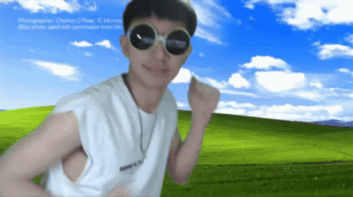 A Man Wearing Round Sunglasses Stands In Front Of A Field GIF
