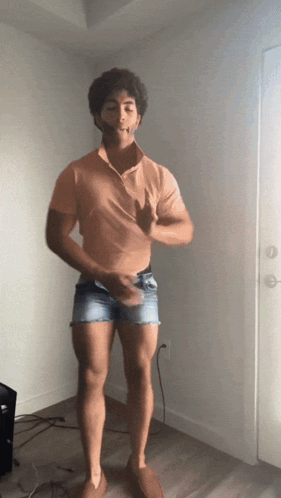 A Man Wearing Shorts And An Orange Shirt Is Standing In Front Of A Door GIF