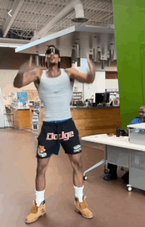 A Man Wearing Shorts That Say Dodge Is Dancing In A Room GIF