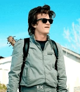A Man Wearing Sunglasses And A Backpack Is Standing In Front Of A House . GIF